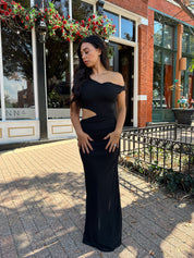 Woman wearing black mesh maxi dress with side cutout, and off the shoulder asymmetrical neckline.