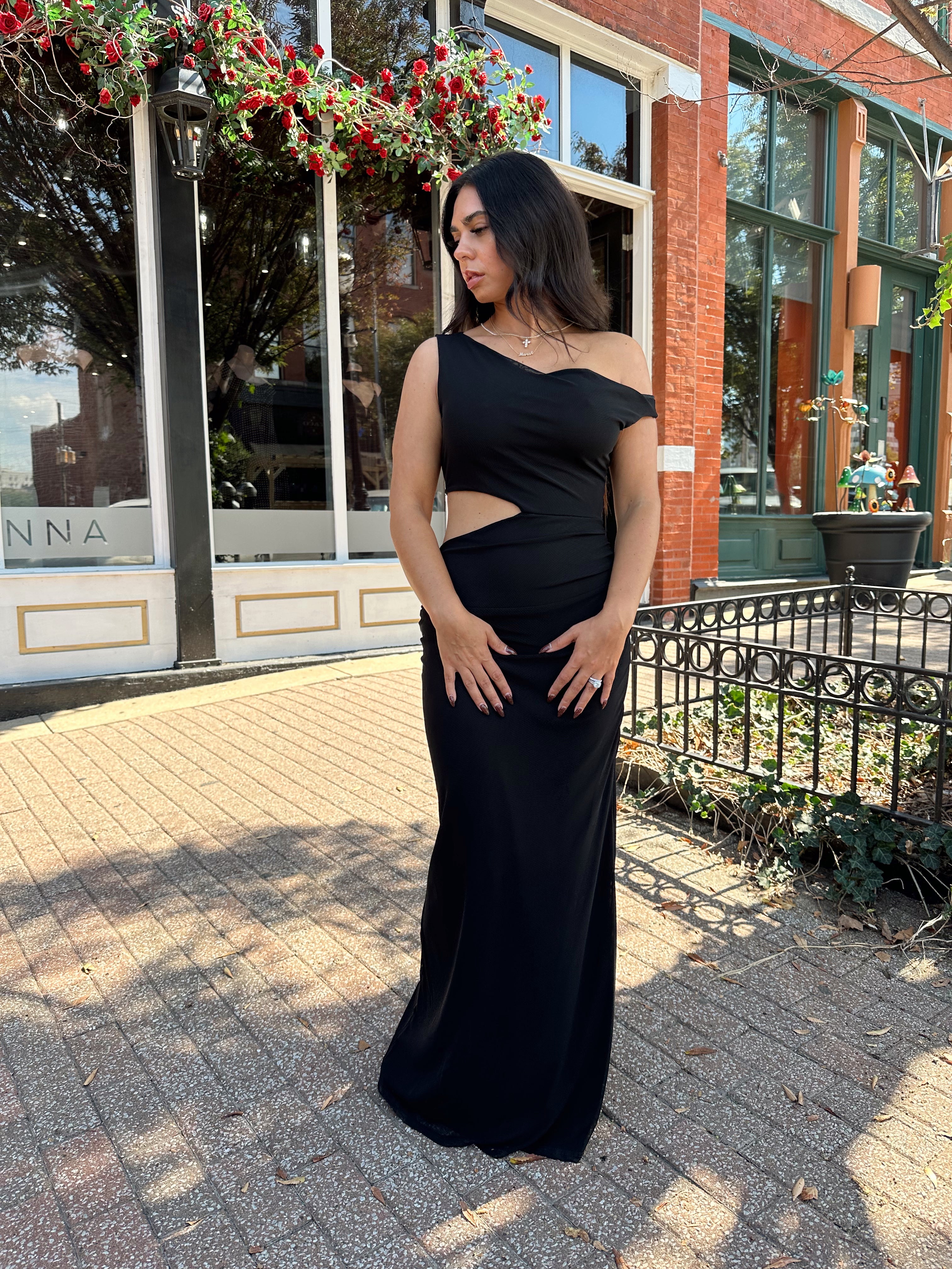 Woman wearing black mesh maxi dress with side cutout, and off the shoulder asymmetrical neckline.