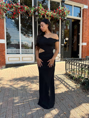 Woman wearing black mesh maxi dress with side cutout, and off the shoulder asymmetrical neckline.