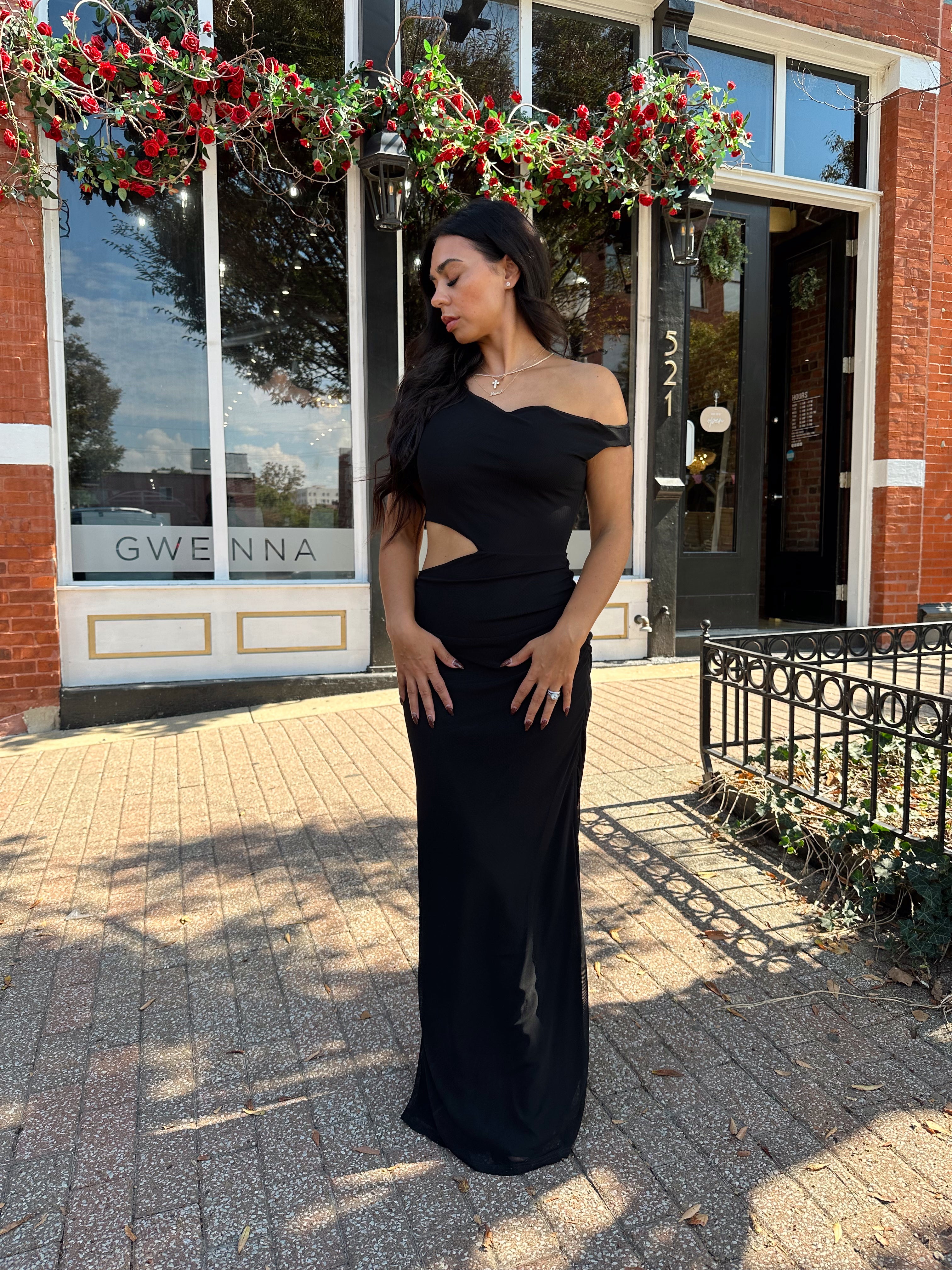Woman wearing black mesh maxi dress with side cutout, and off the shoulder asymmetrical neckline.