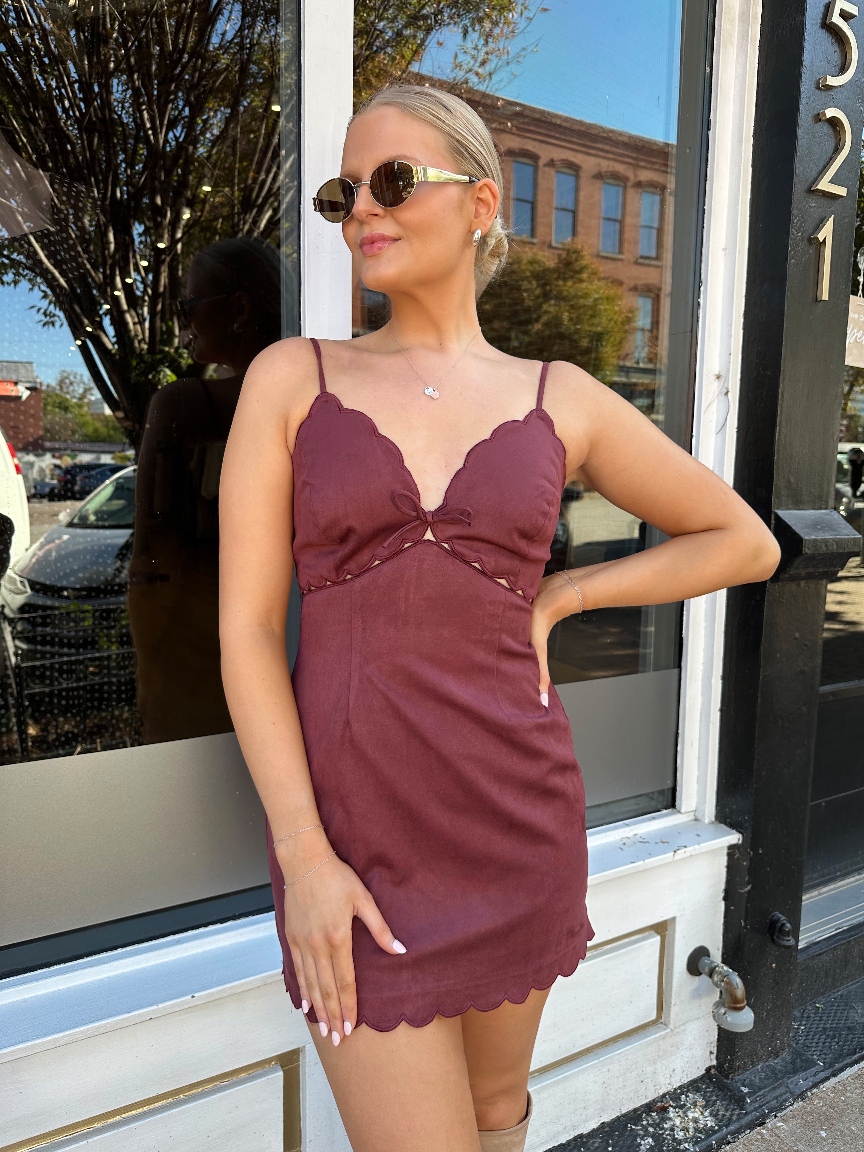 Woman wearing burgundy suede mini dress with scallop detail.
