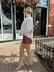 Woman wearing burgundy leather mini dress with stone knit turtle neck sweater.
