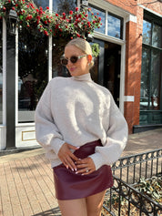 Woman wearing burgundy leather mini dress with stone knit turtle neck sweater.