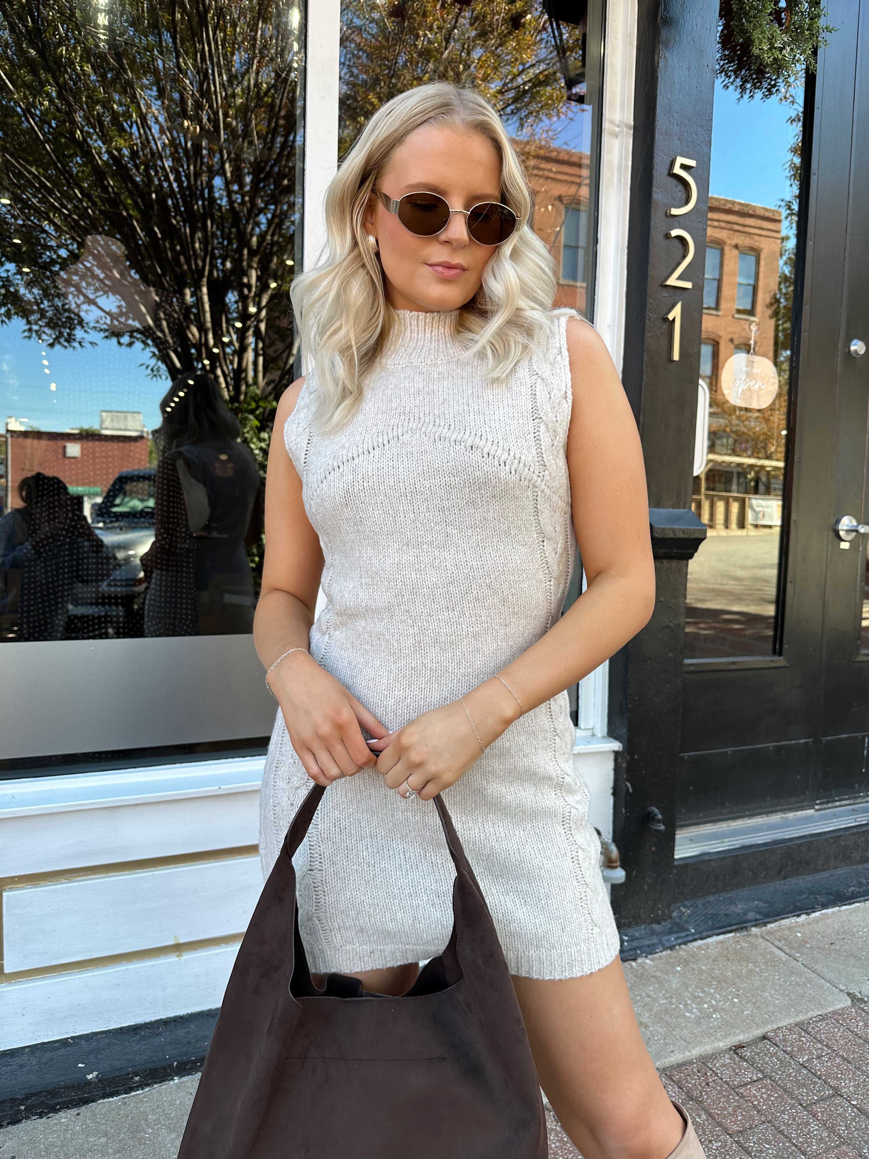 Woman wearing oatmeal colored sleeveless sweater dress with suede knee boots.