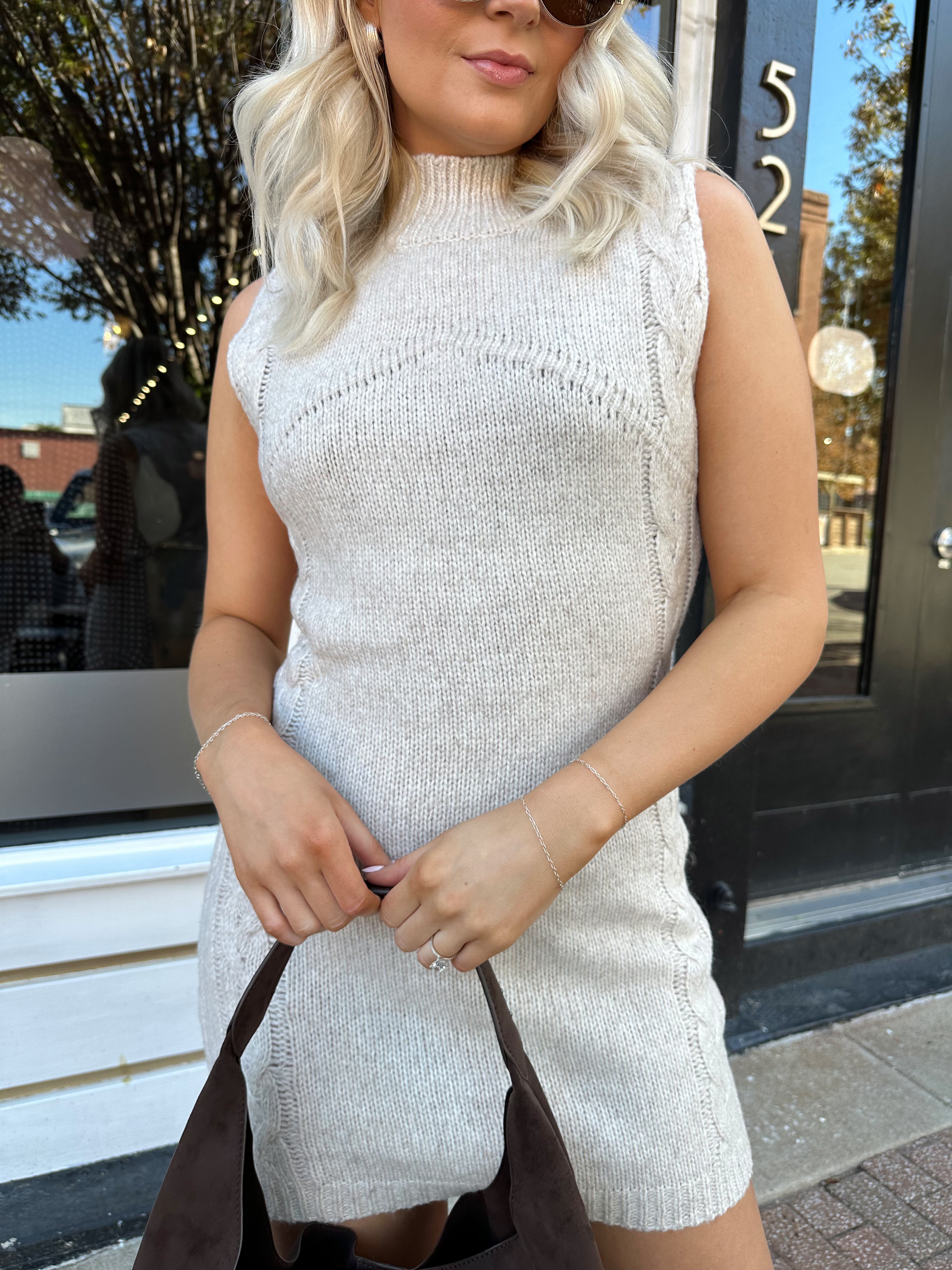Woman wearing oatmeal colored sleeveless sweater dress with suede knee boots.