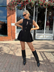 Woman wearing fit to flare black mini dress with keyhole cutout and gold buttons.