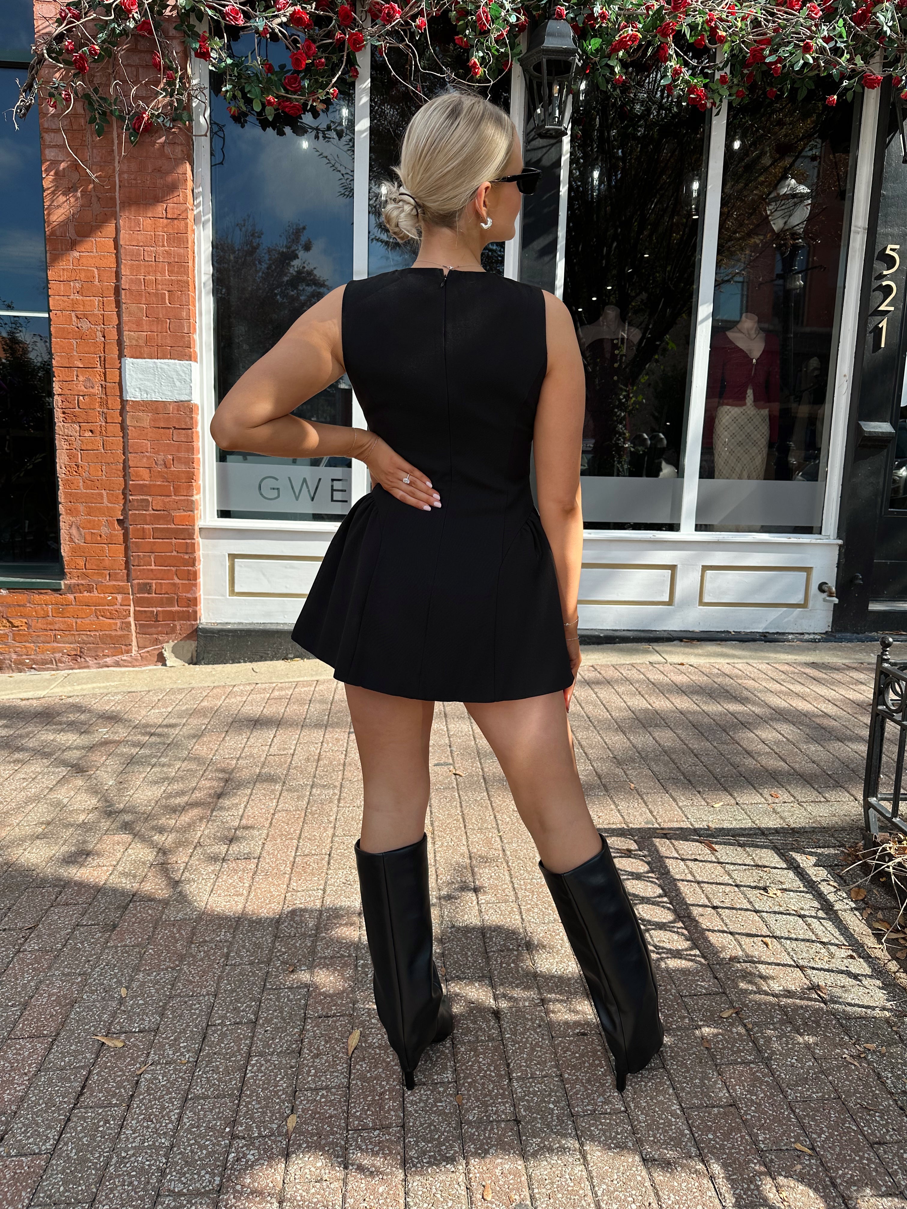 Woman wearing fit to flare black mini dress with keyhole cutout and gold buttons.