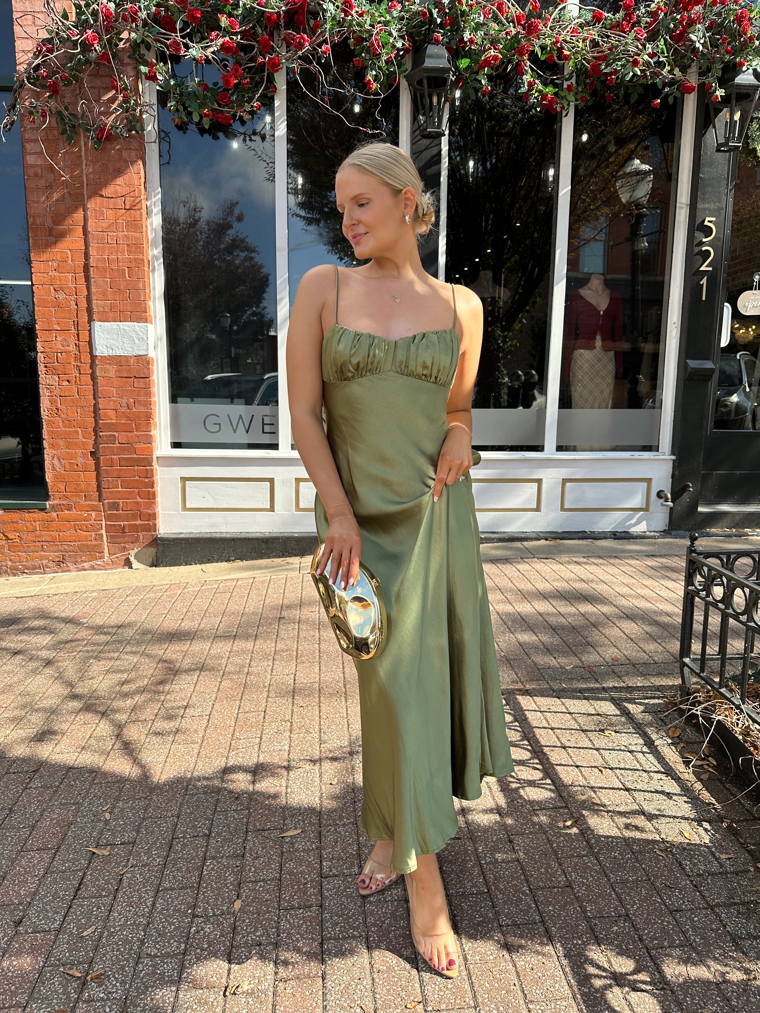Woman wearing olive green satin maxi dress with open twist back.