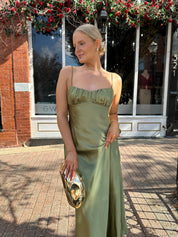 Woman wearing olive green satin maxi dress with open twist back.