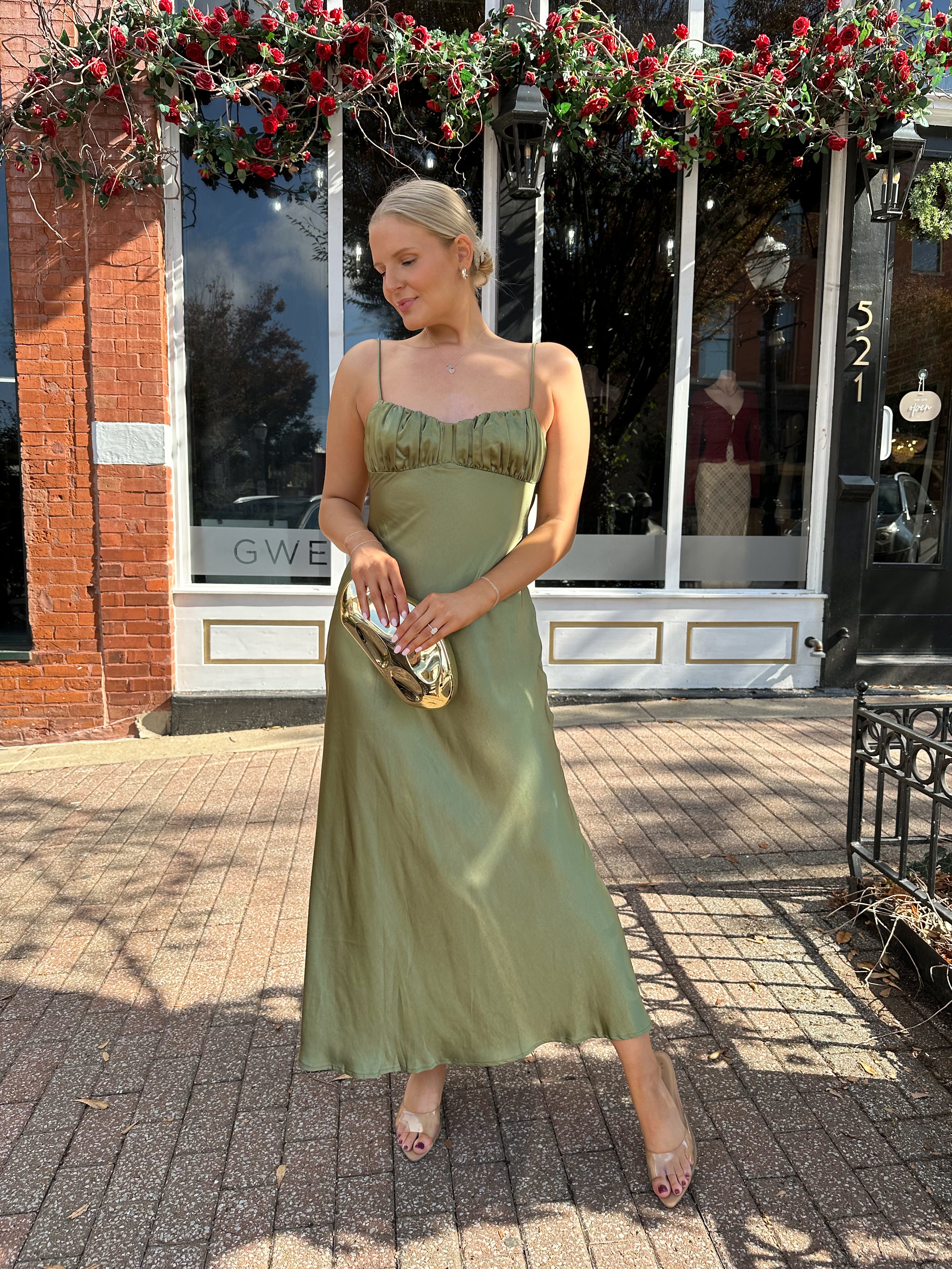 Woman wearing olive green satin maxi dress with open twist back.