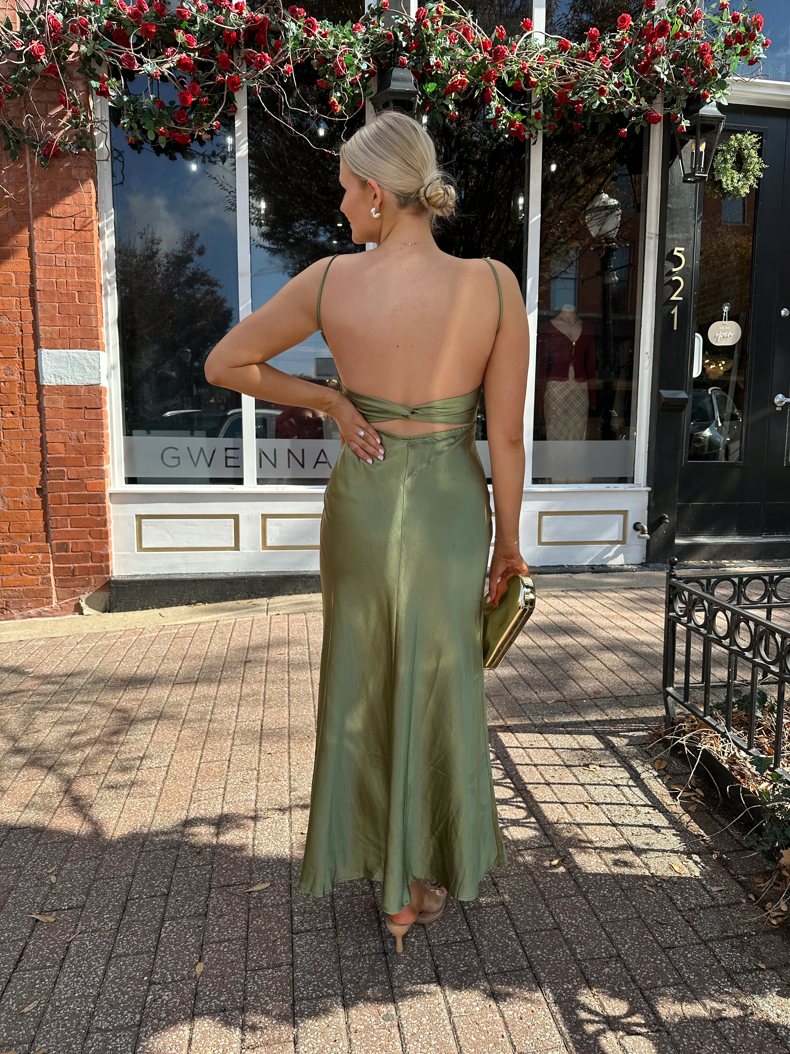 Woman wearing olive green satin maxi dress with open twist back.