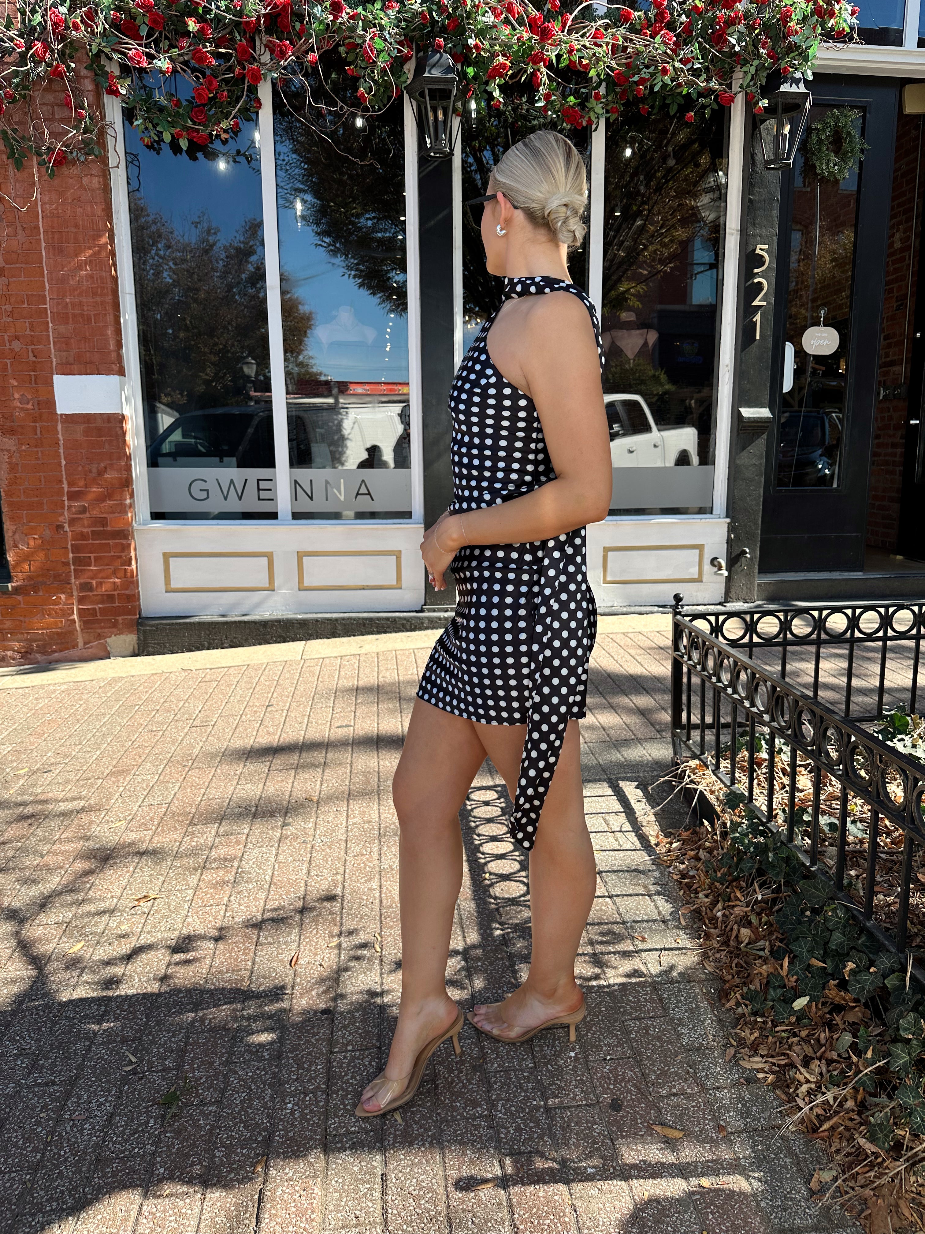 Woman wearing black and white polka dot satin mini dress with halter scarf neckline.