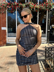 Woman wearing black and white polka dot satin mini dress with halter scarf neckline.
