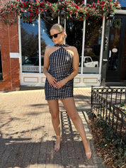 Woman wearing black and white polka dot satin mini dress with halter scarf neckline.