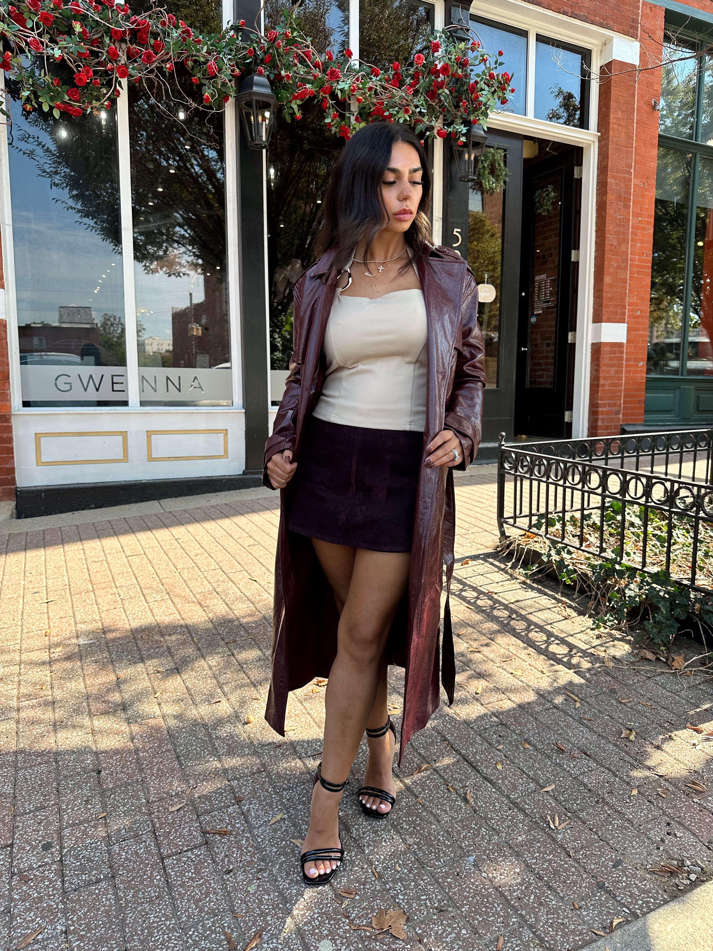 Woman wearing burgundy leather trench coat with belt and and button closure.