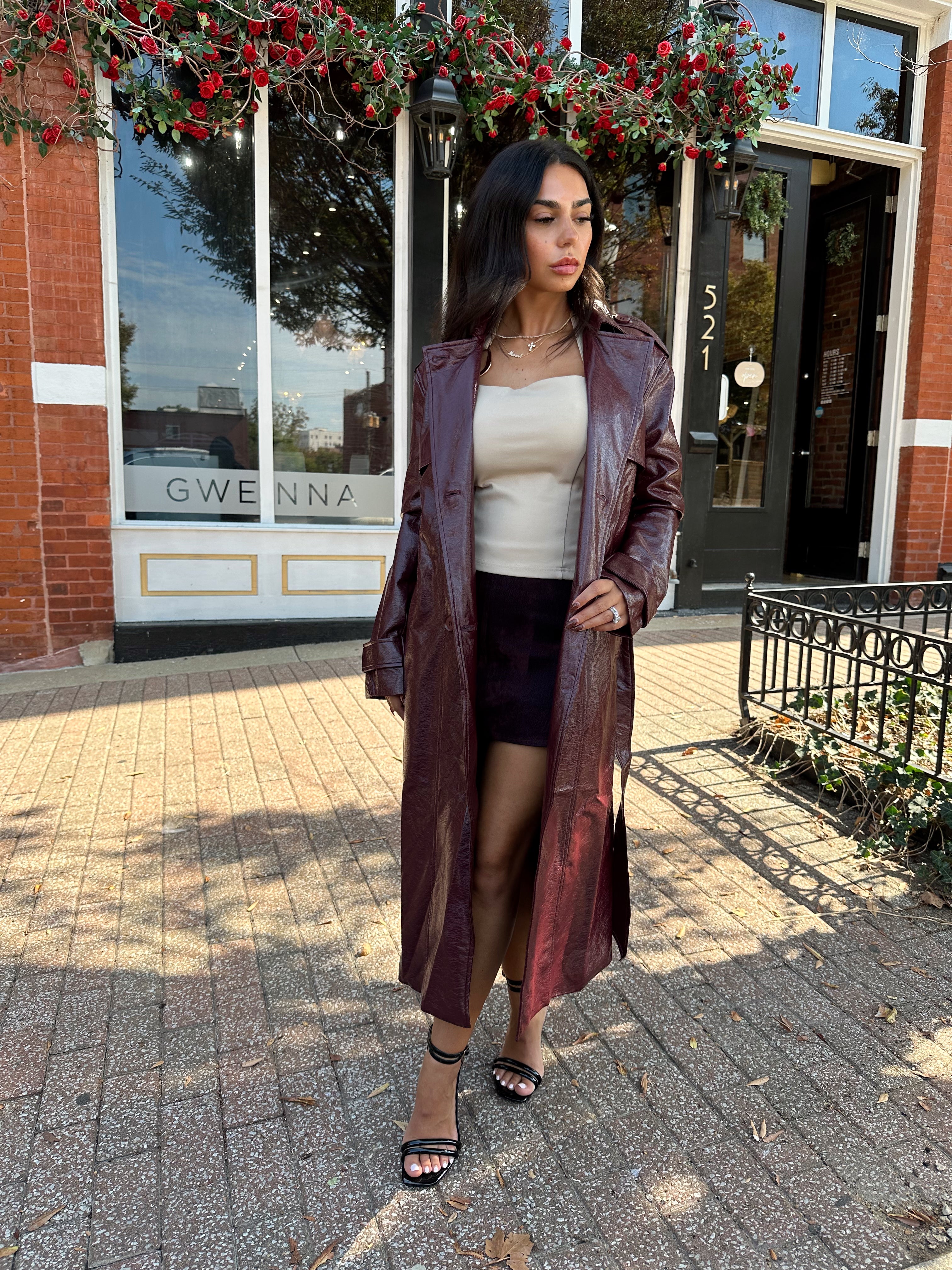 Woman wearing burgundy leather trench coat with belt and and button closure.