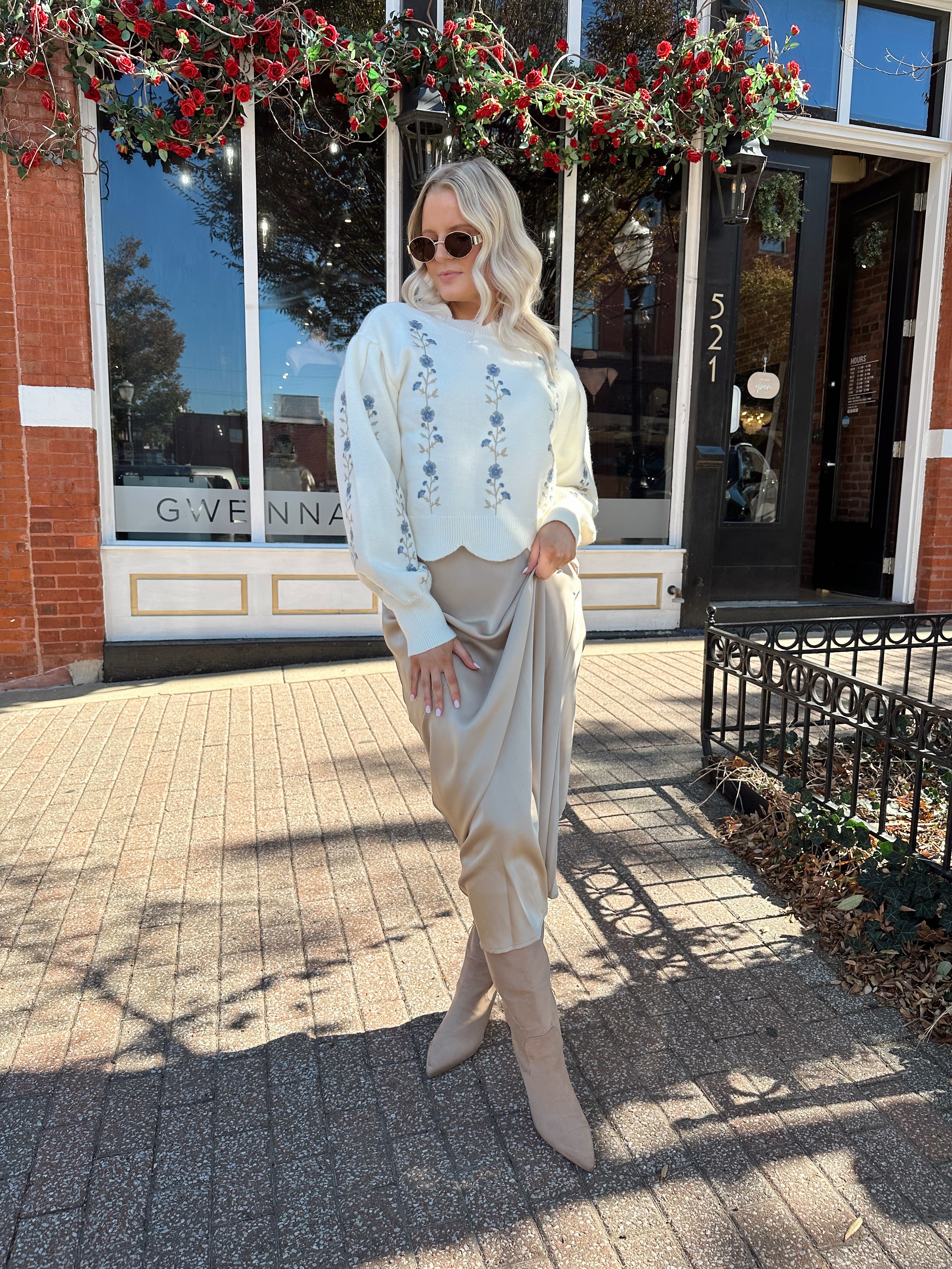 Woman wearing cream sweater with blue embroidered floral pattern.