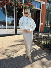 Woman wearing cream sweater with blue embroidered floral pattern.