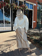 Woman wearing cream sweater with blue embroidered floral pattern.