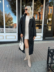 Woman wearing black tailored trench coat and knit sweater mini dress.