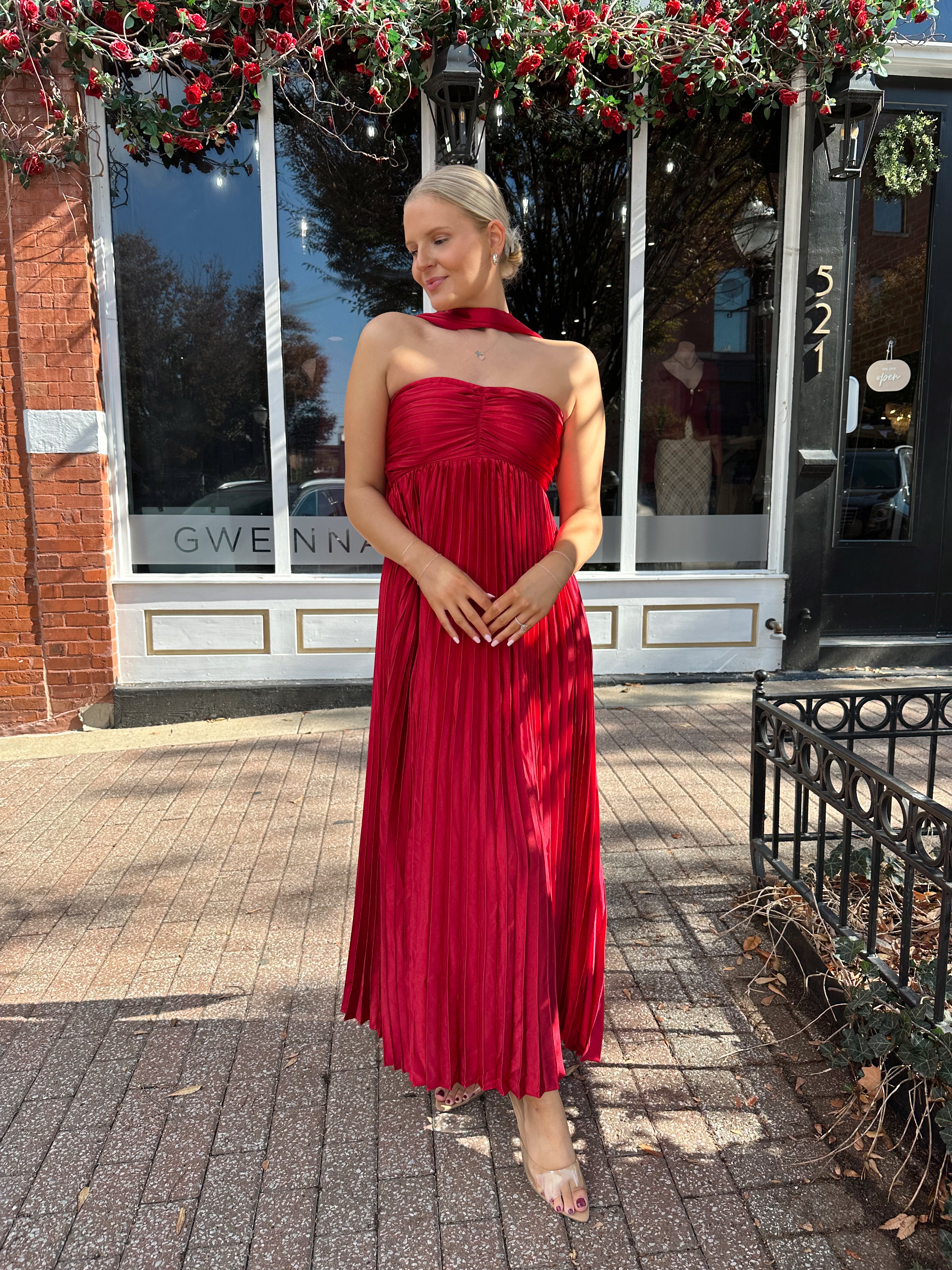 Woman wearing strapless red plissé maxi dress with lace up back, and detachable scarf.
