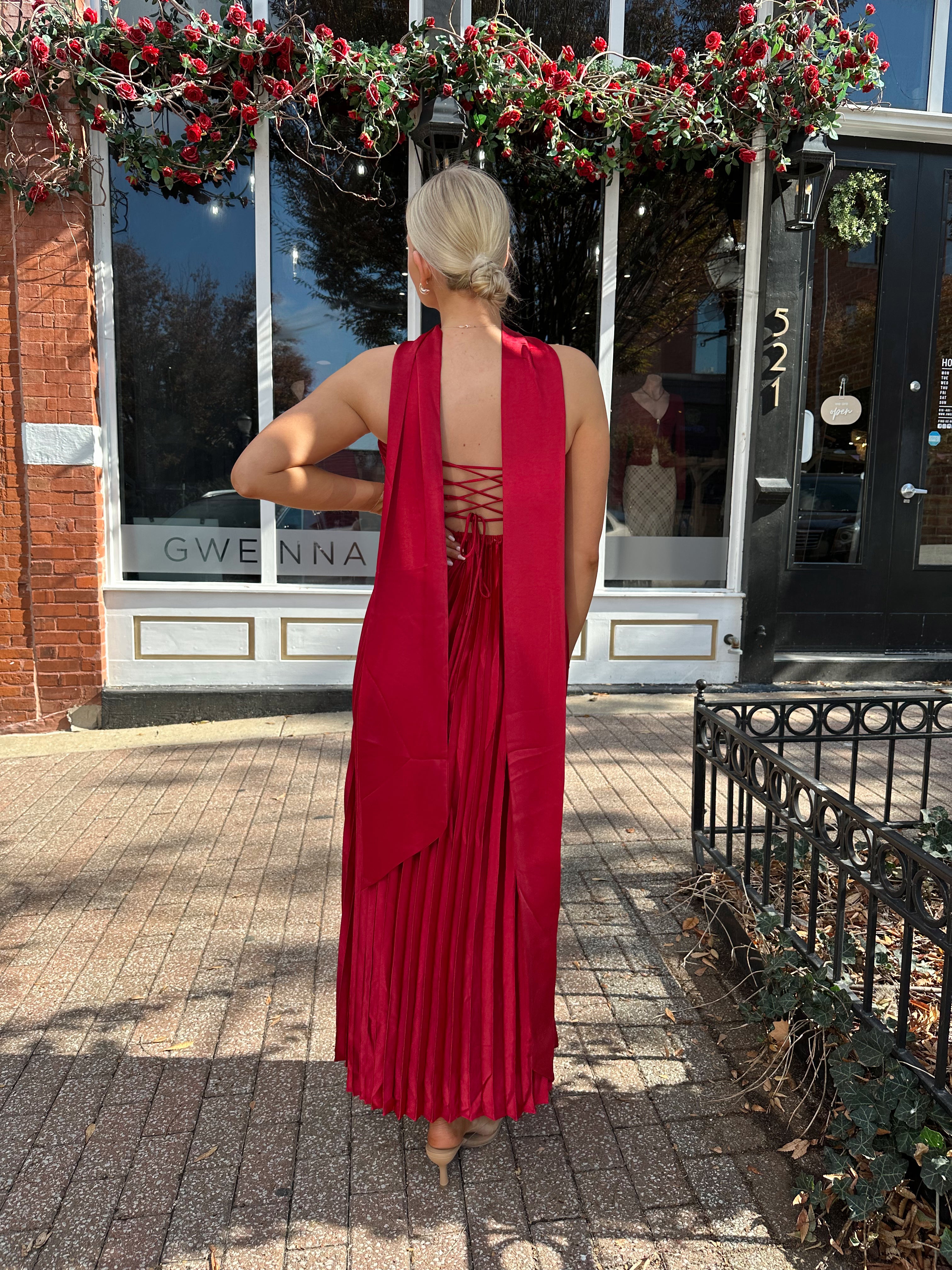 Woman wearing strapless red plissé maxi dress with lace up back, and detachable scarf.