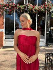 Woman wearing strapless red plissé maxi dress with lace up back, and detachable scarf.