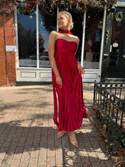 Woman wearing strapless red plissé maxi dress with lace up back, and detachable scarf.