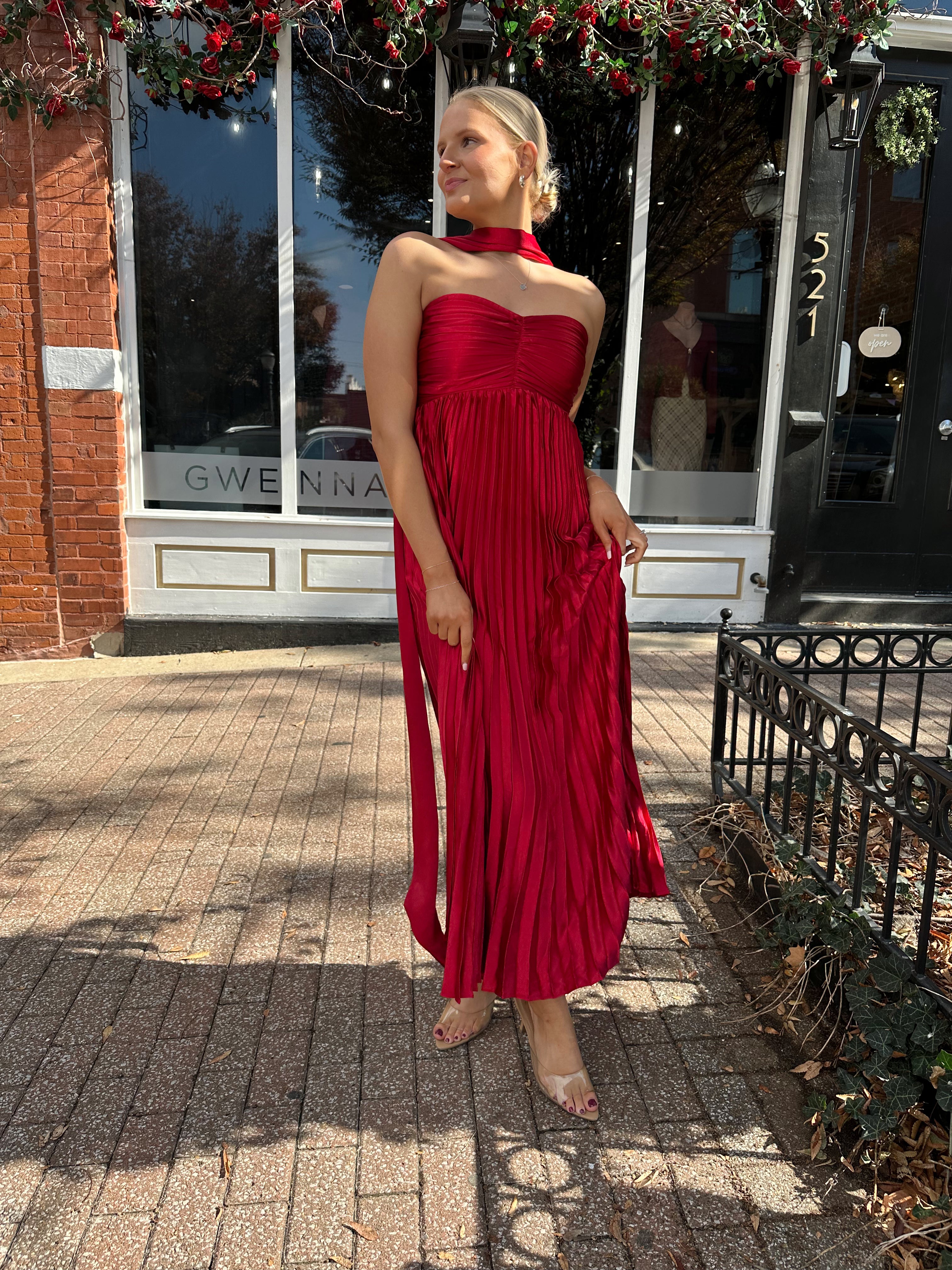 Woman wearing strapless red plissé maxi dress with lace up back, and detachable scarf.