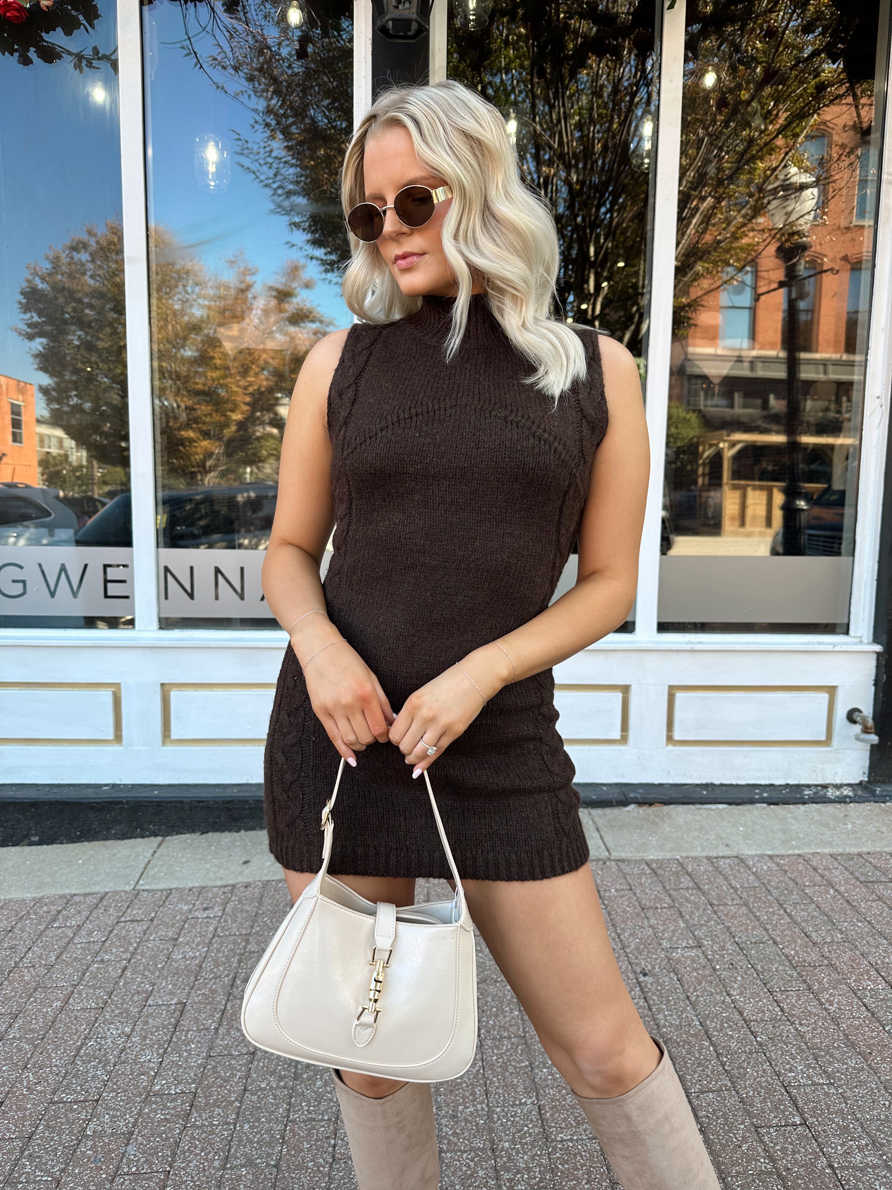 Woman wearing dark brown sleeveless sweater dress with suede knee boot.