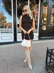 Woman wearing dark brown sleeveless sweater dress with suede knee boot.