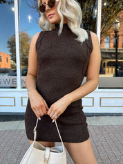 Woman wearing dark brown sleeveless sweater dress with suede knee boot.
