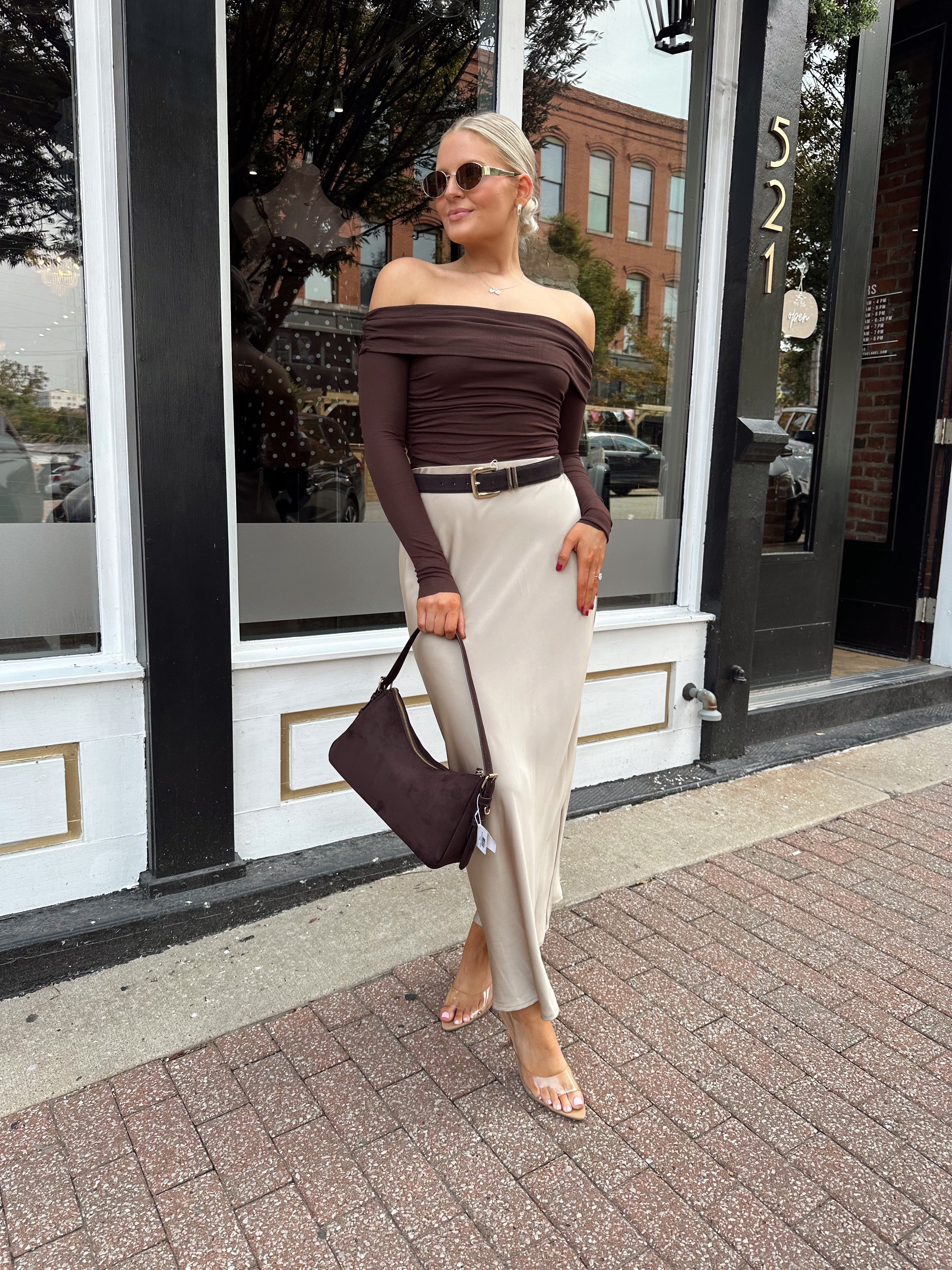 Woman wearing tan satin maxi skirt with elastic waist band and brown off the shoulder bodysuit.