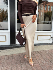 Woman wearing tan satin maxi skirt with elastic waist band and brown off the shoulder bodysuit.