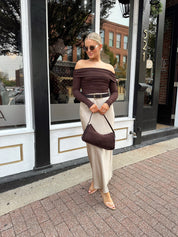 Woman wearing tan satin maxi skirt with elastic waist band and brown off the shoulder bodysuit.