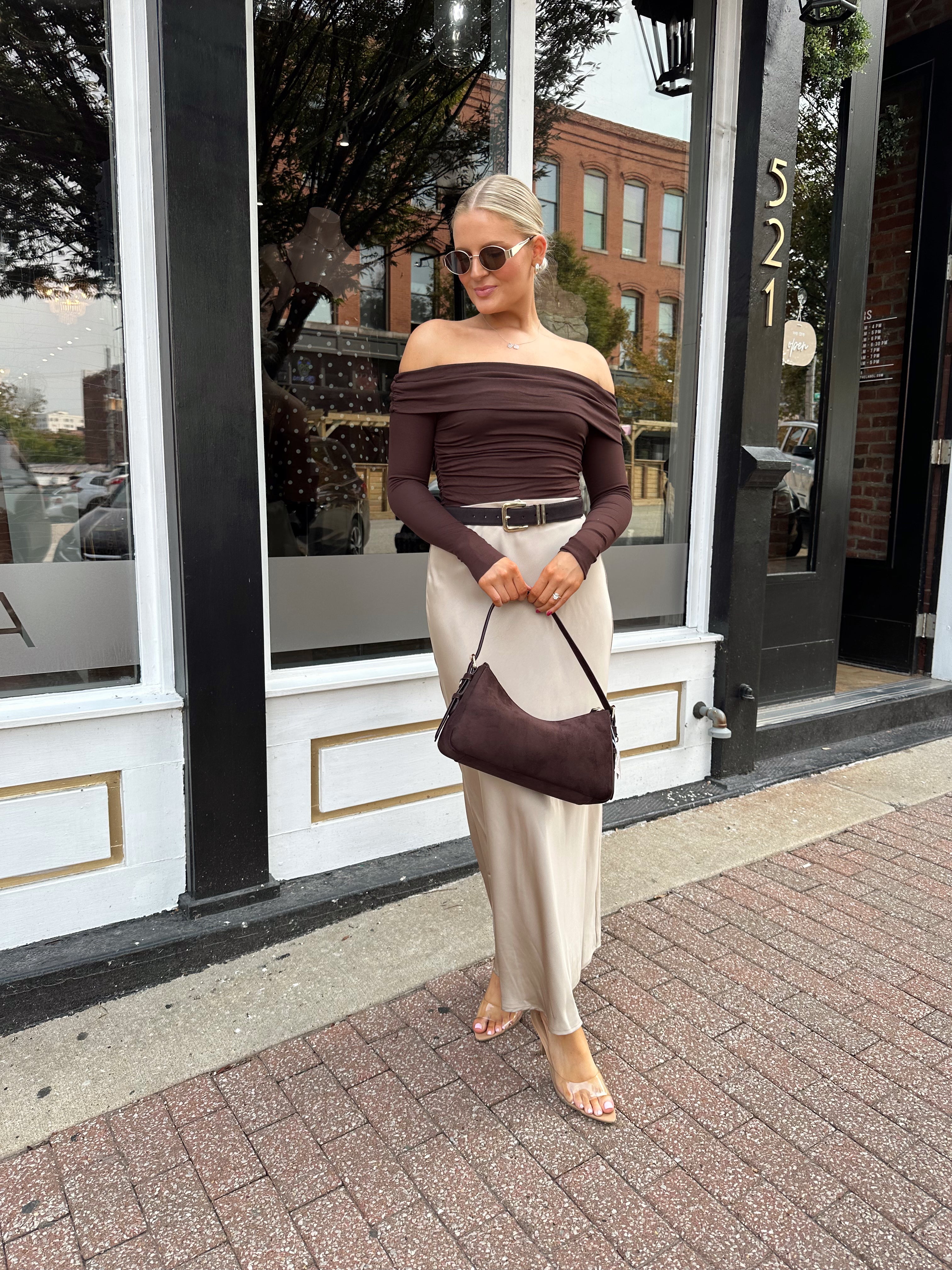 Woman wearing tan satin maxi skirt with elastic waist band and brown off the shoulder bodysuit.