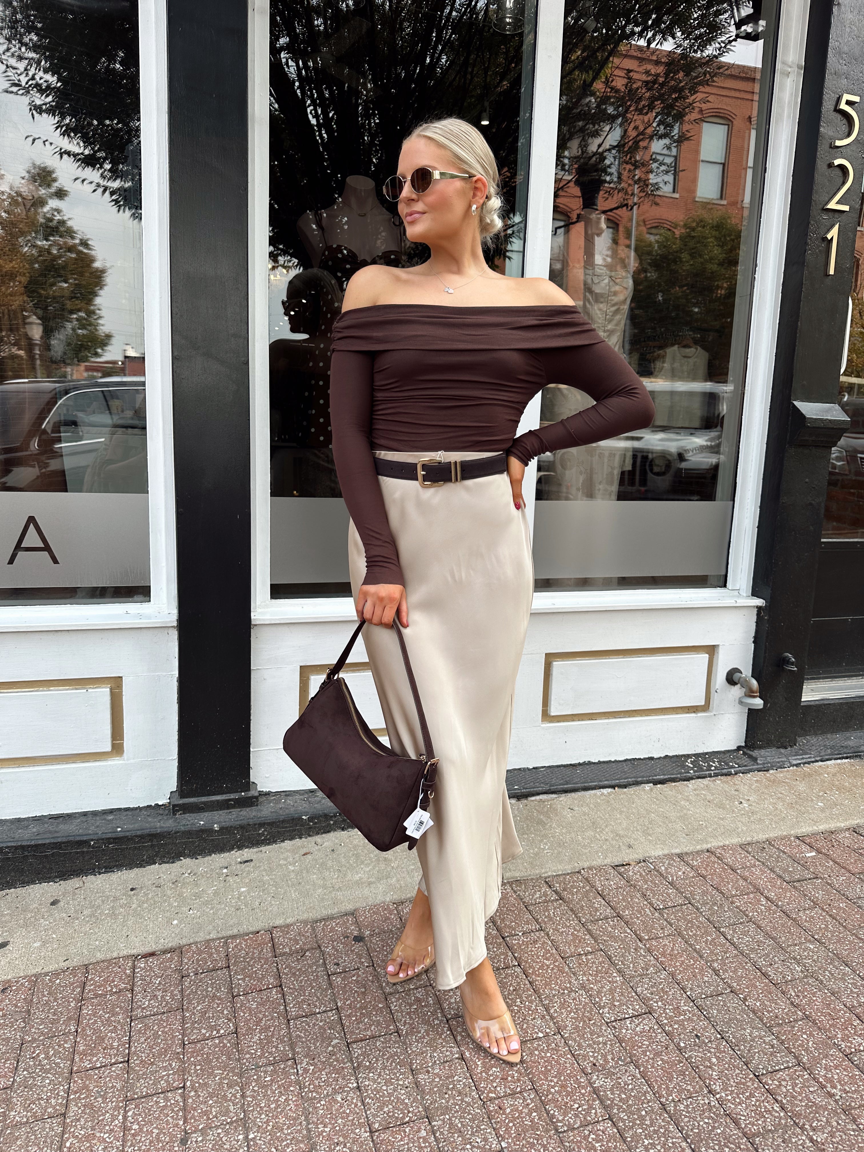 Woman wearing tan satin maxi skirt with elastic waist band and brown off the shoulder bodysuit.