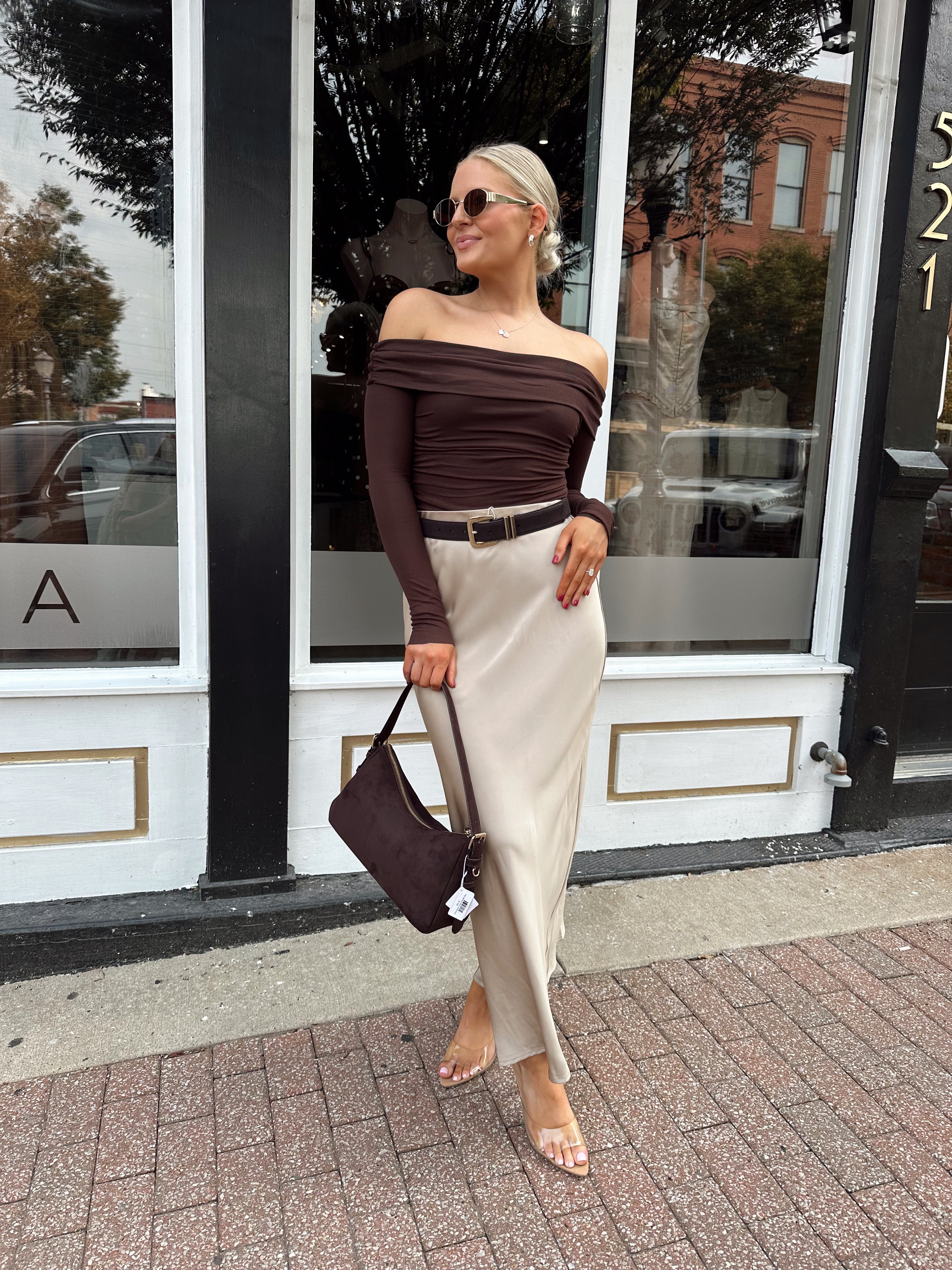 Woman wearing tan satin maxi skirt with elastic waist band and brown off the shoulder bodysuit.