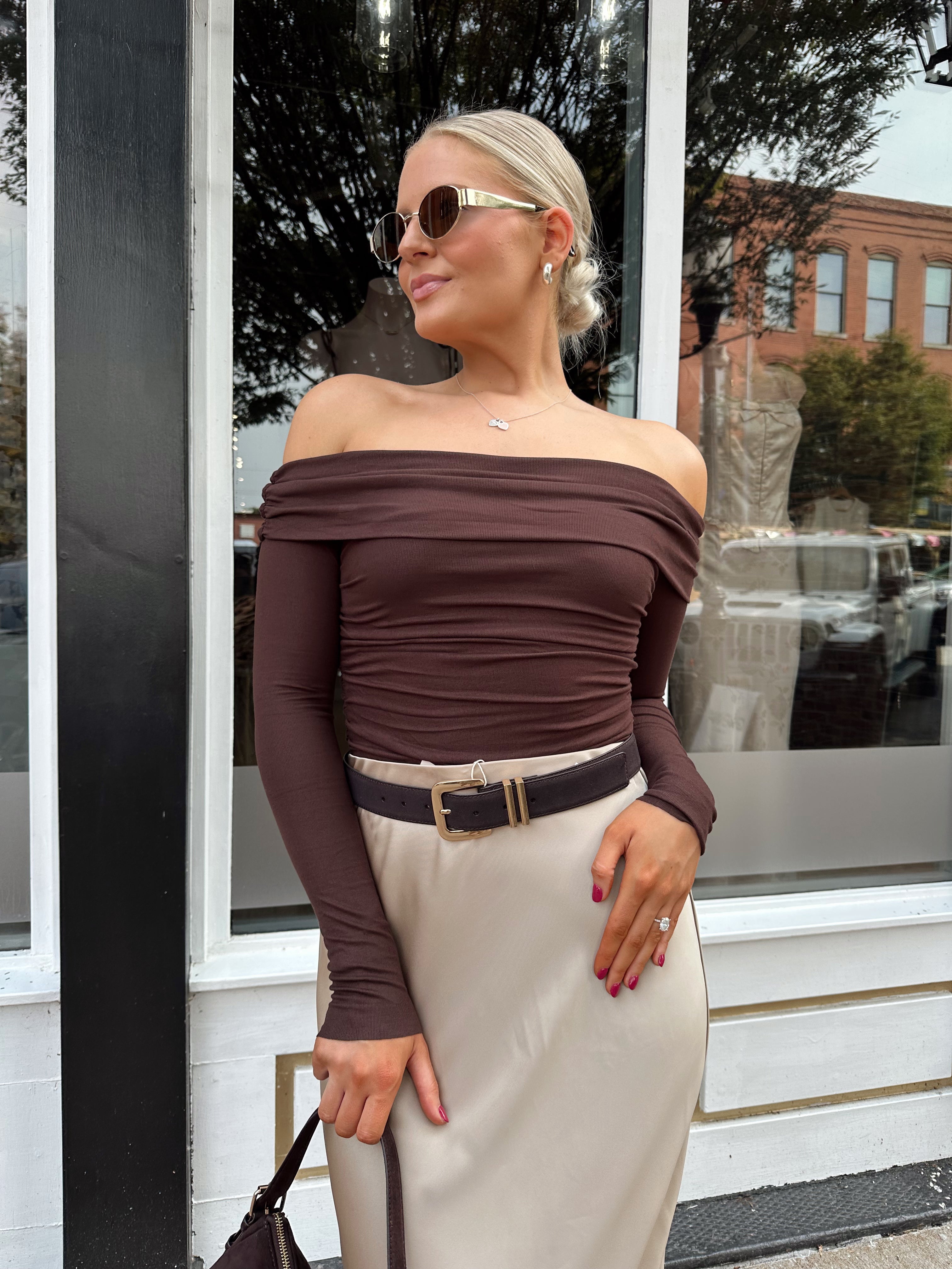 Woman wearing tan satin maxi skirt with elastic waist band and brown off the shoulder bodysuit.