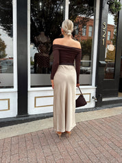 Woman wearing tan satin maxi skirt with elastic waist band and brown off the shoulder bodysuit.