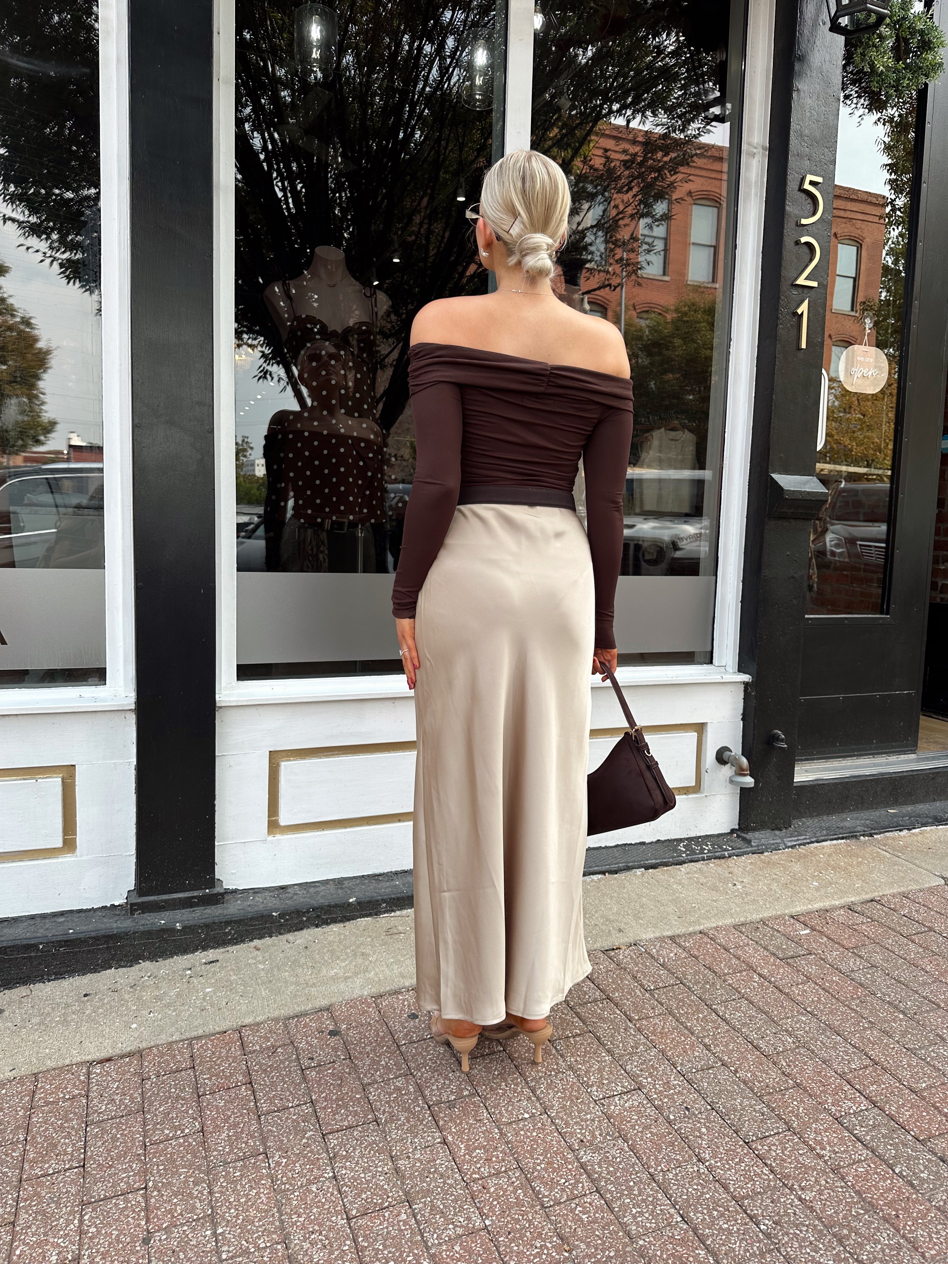Woman wearing tan satin maxi skirt with elastic waist band and brown off the shoulder bodysuit.