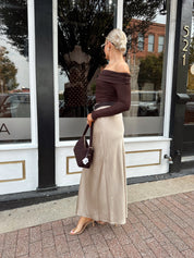 Woman wearing tan satin maxi skirt with elastic waist band and brown off the shoulder bodysuit.