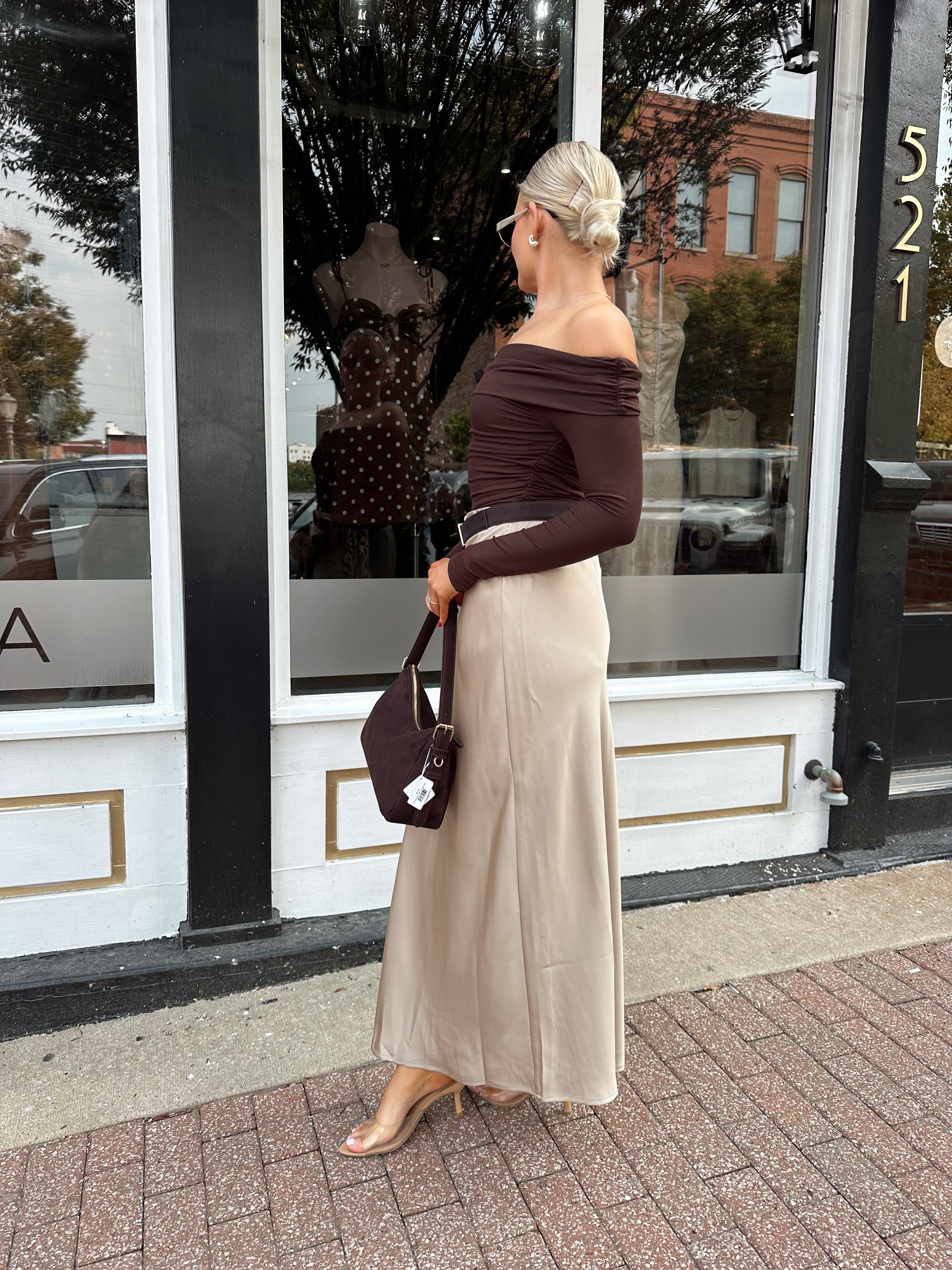 Woman wearing tan satin maxi skirt with elastic waist band and brown off the shoulder bodysuit.