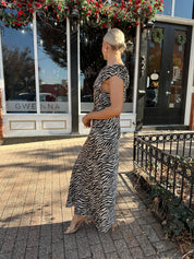 Woman wearing zebra print satin maxi dress with asymmetrical neckline.