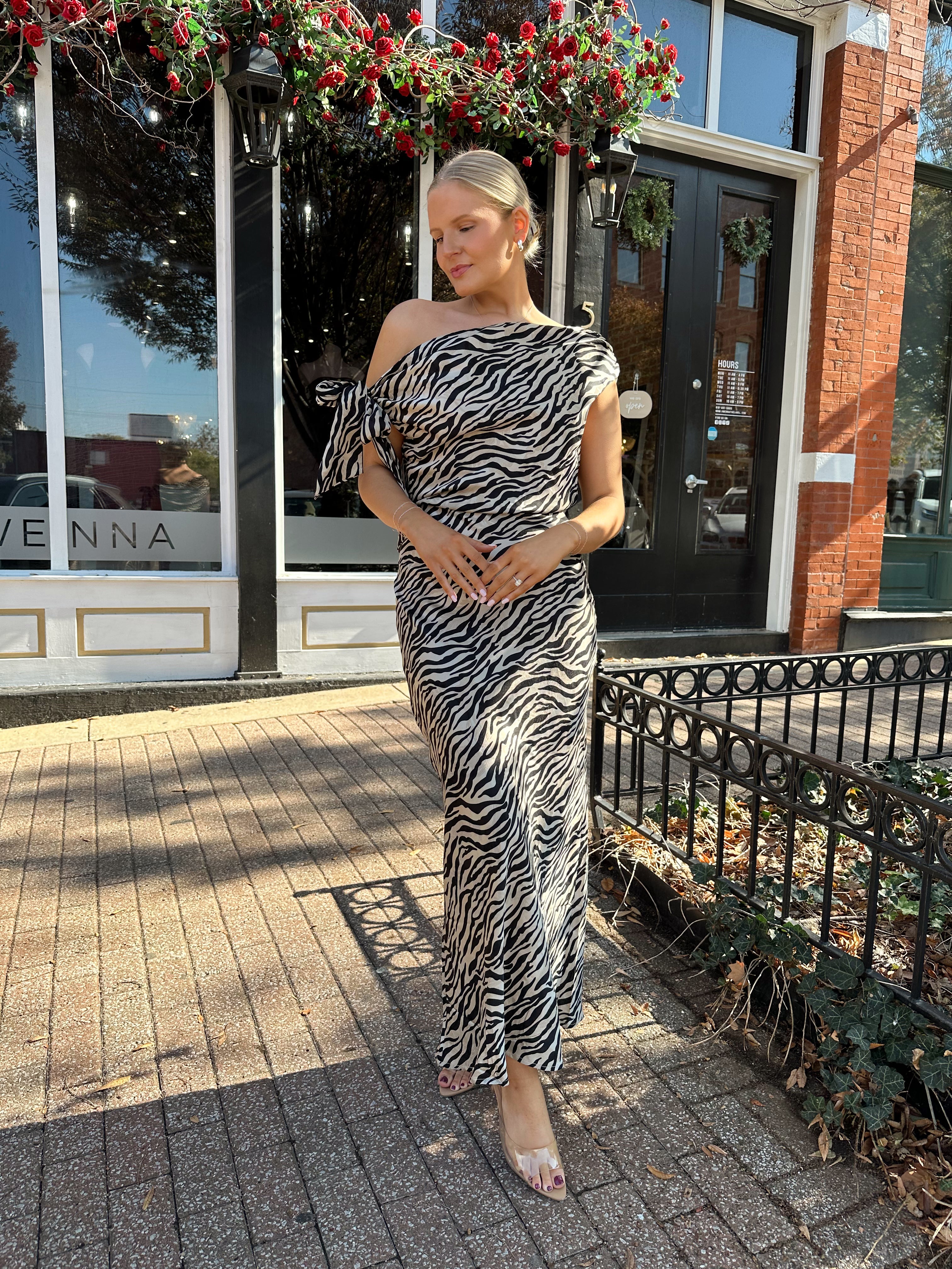 Woman wearing zebra print satin maxi dress with asymmetrical neckline.