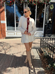 Woman wearing cream front tie cardigan with burgundy stitch detailing.