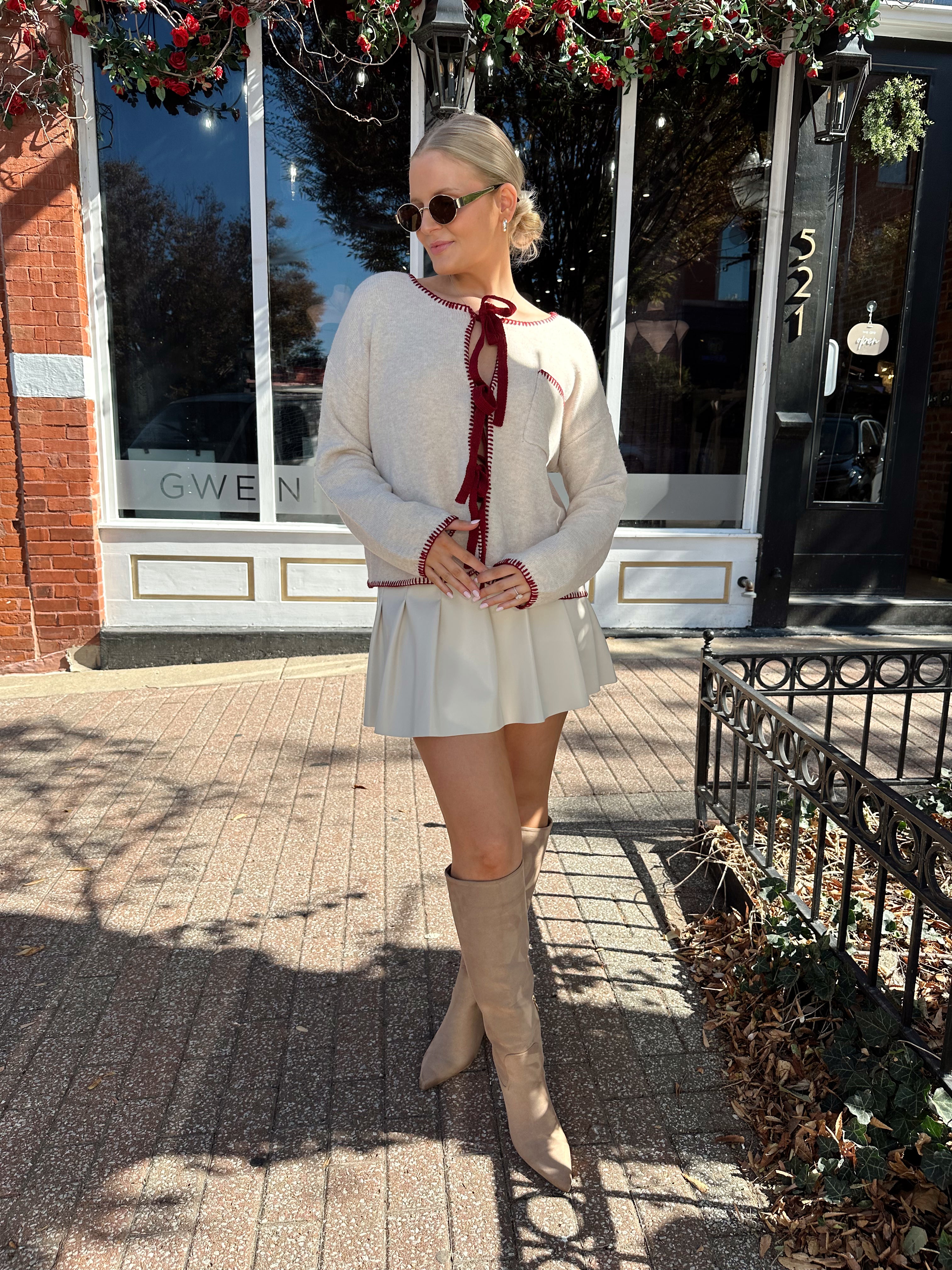 Woman wearing cream front tie cardigan with burgundy stitch detailing.