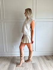 Woman wearing a cream vegan leather pleated mini skirt and oatmeal knit sleeveless top.