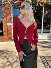 Woman wearing burgundy long sleeve top with twist front and gold detail.