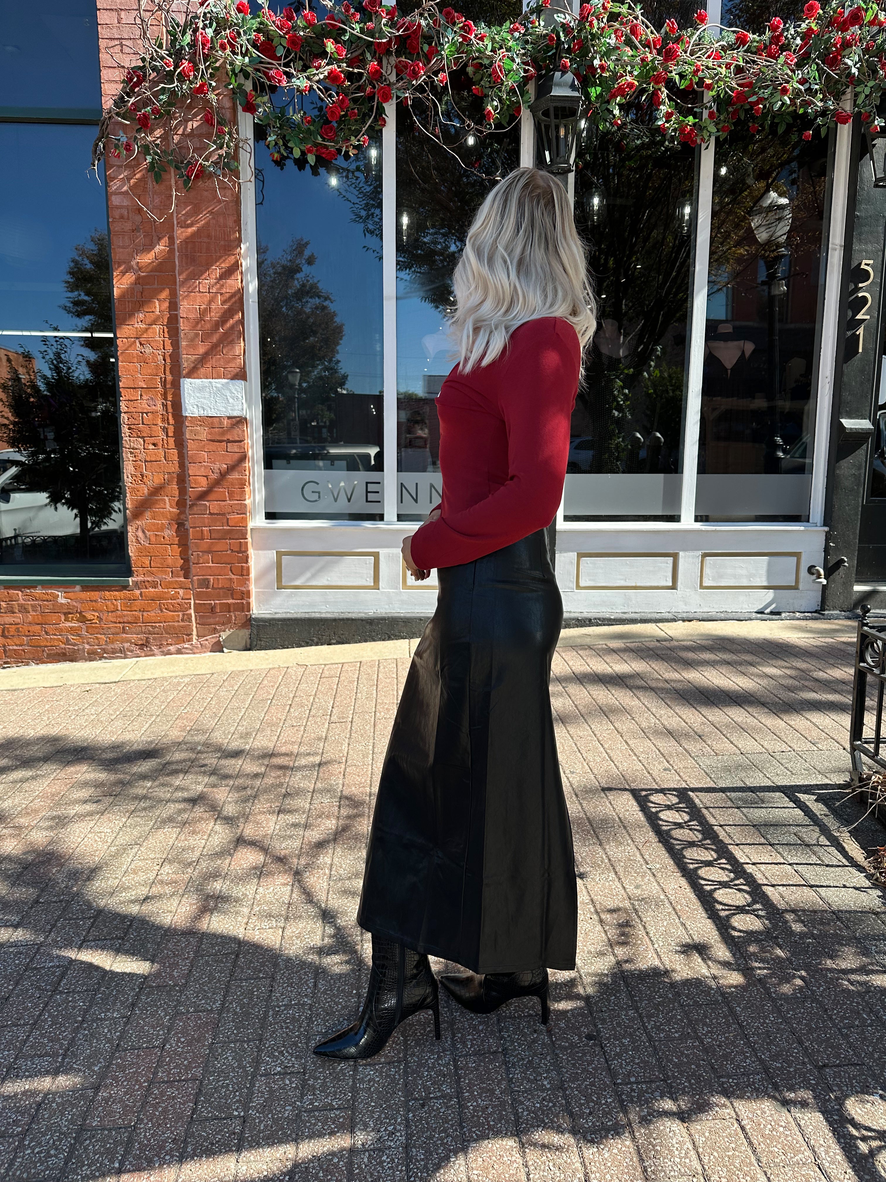 Woman wearing burgundy long sleeve top with twist front and gold detail.